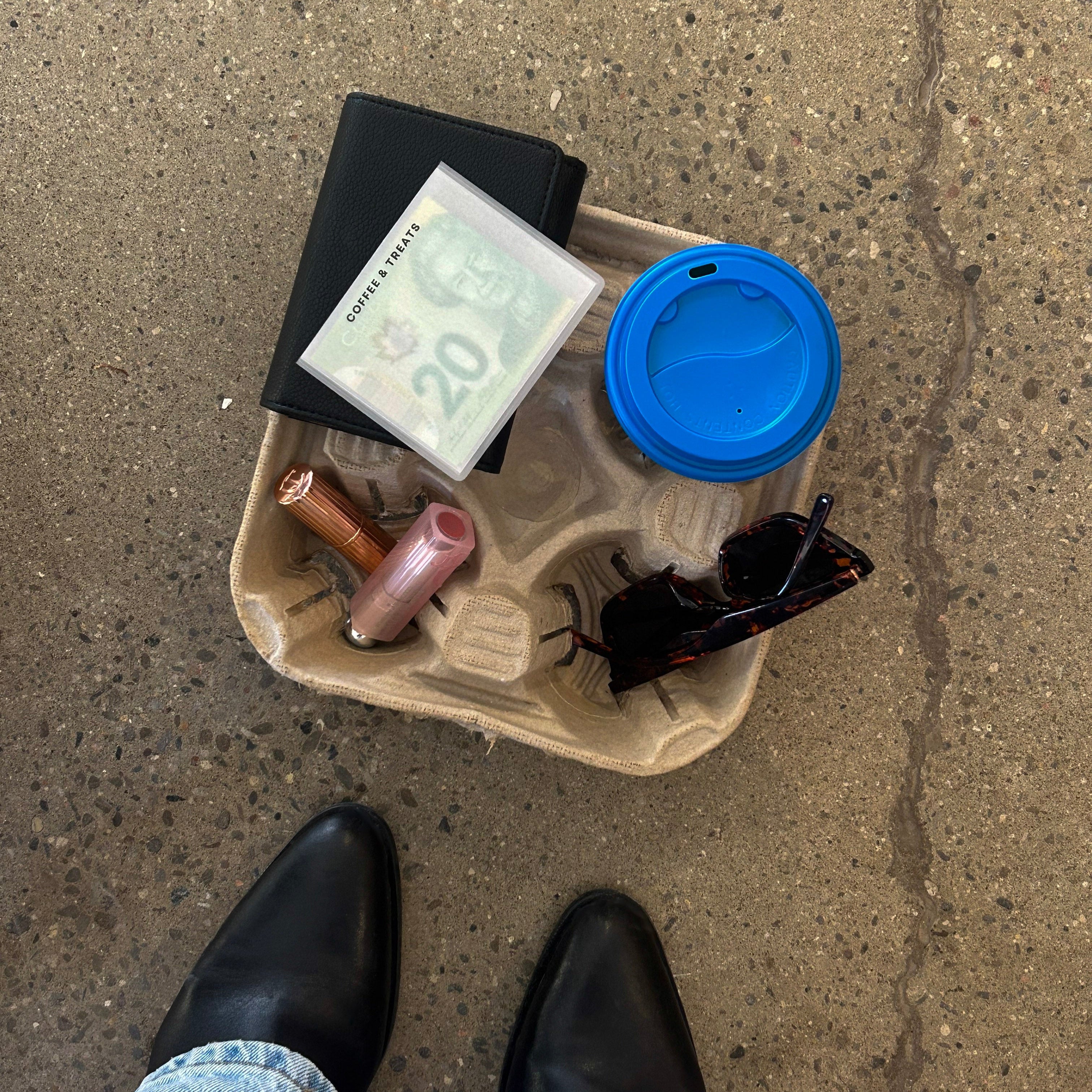 Coffee tray with sunglasses, coffee cup, lipsticks, black wallet, and cash envelopes.