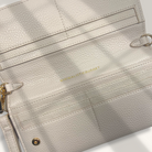 Close-up of a light gray leather clutch with gold accents on a white background