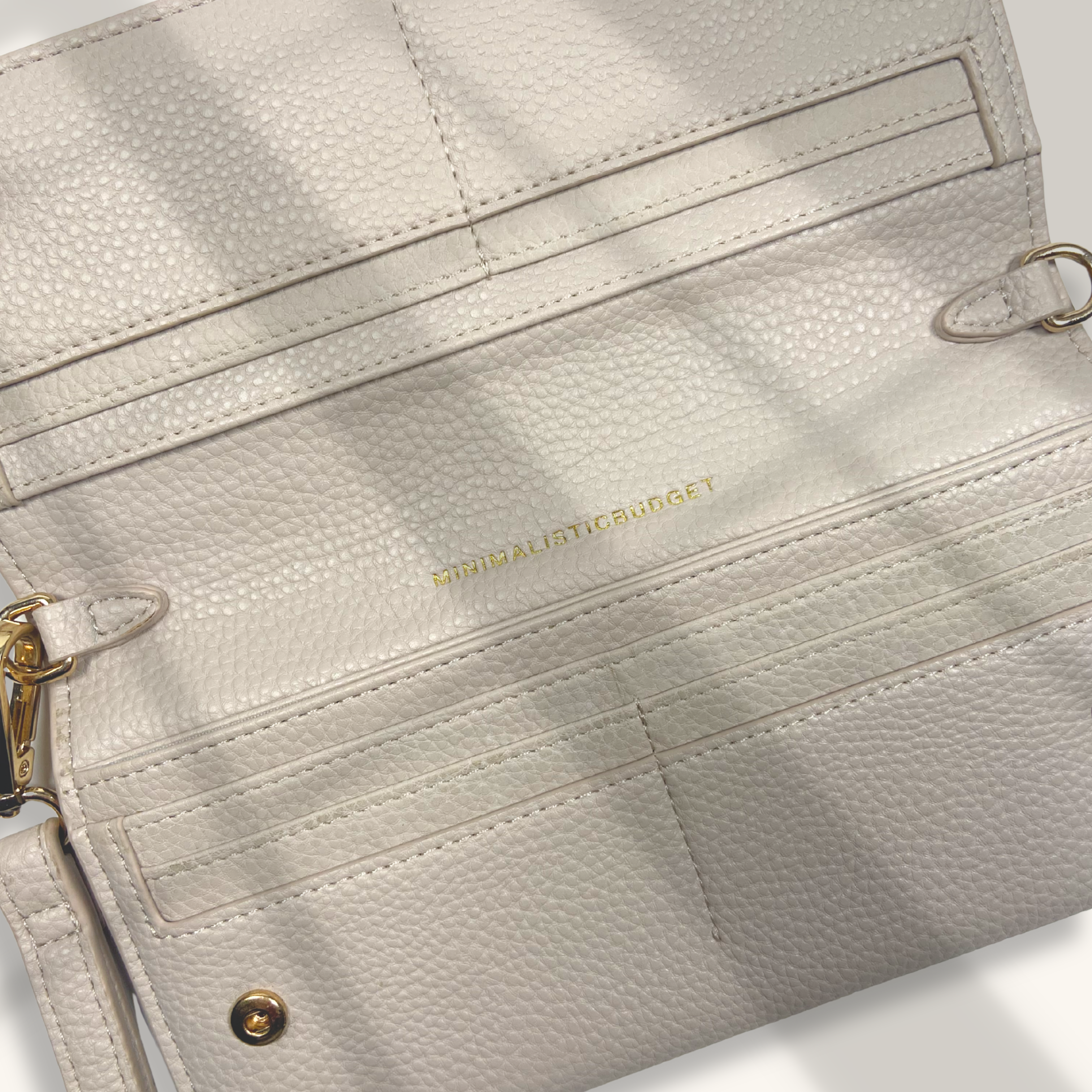 Close-up of a light gray leather clutch with gold accents on a white background