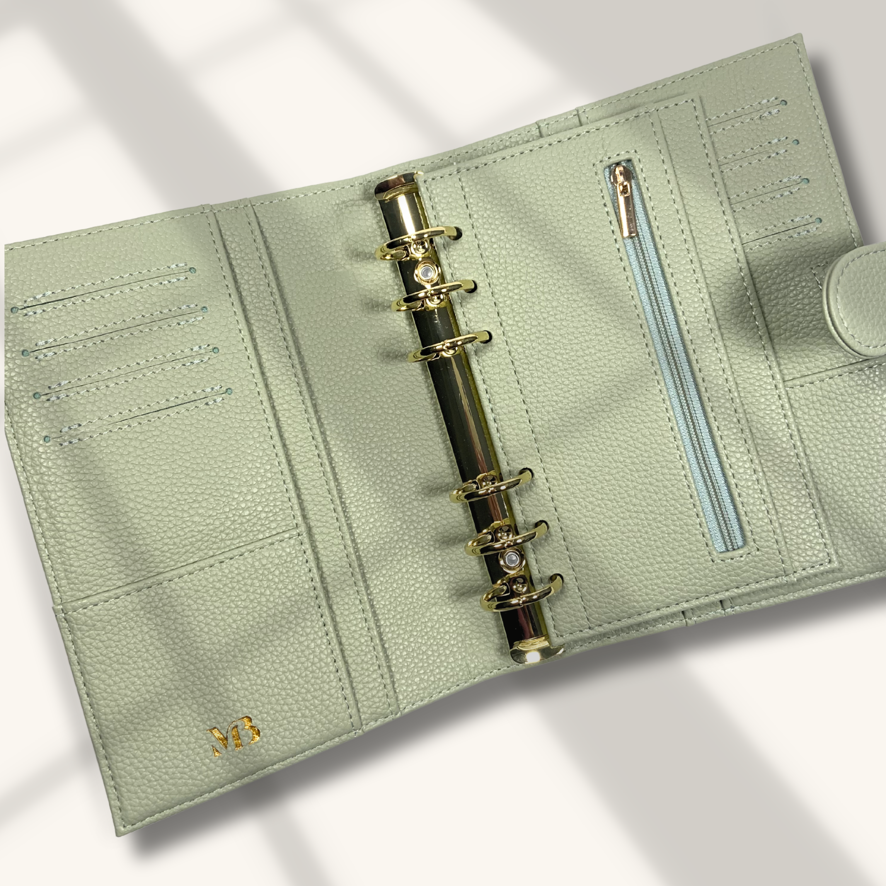 Light green leather planner with gold rings on a light gray background