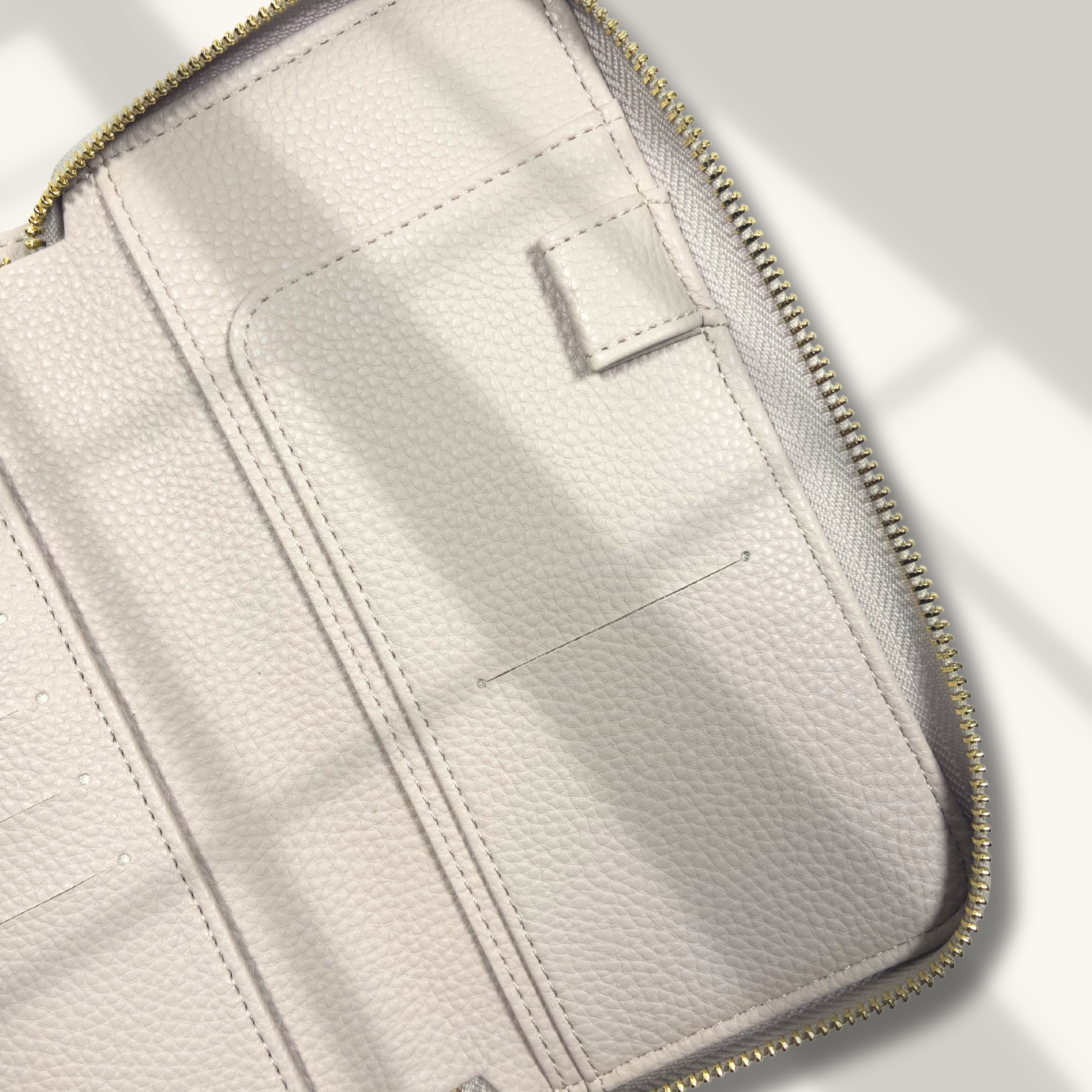 Close-up of a light beige leather wallet with gold zipper on a white background