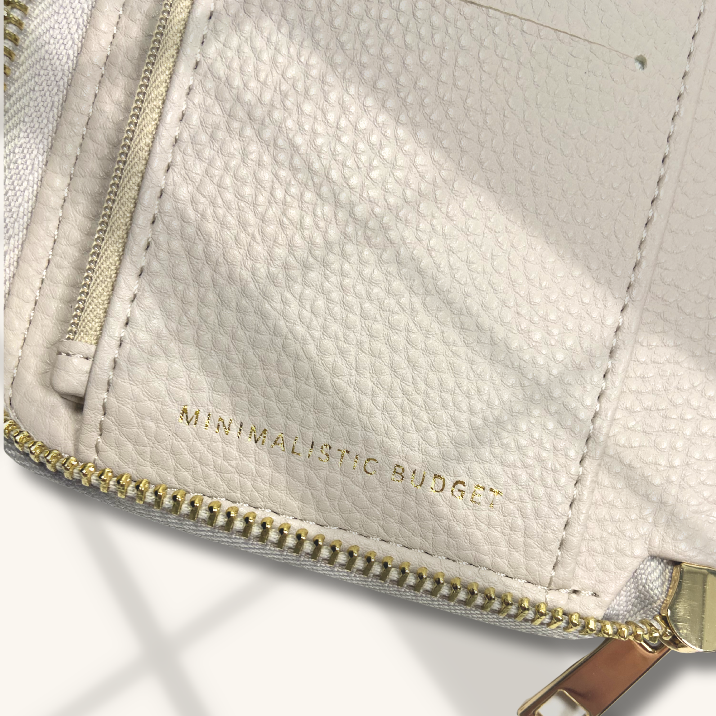 Close-up of a beige textured wallet with gold zipper and 'Minimalistic Budget' text on a white background