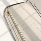 Close-up of a beige leather wallet with a gold zipper on a light background