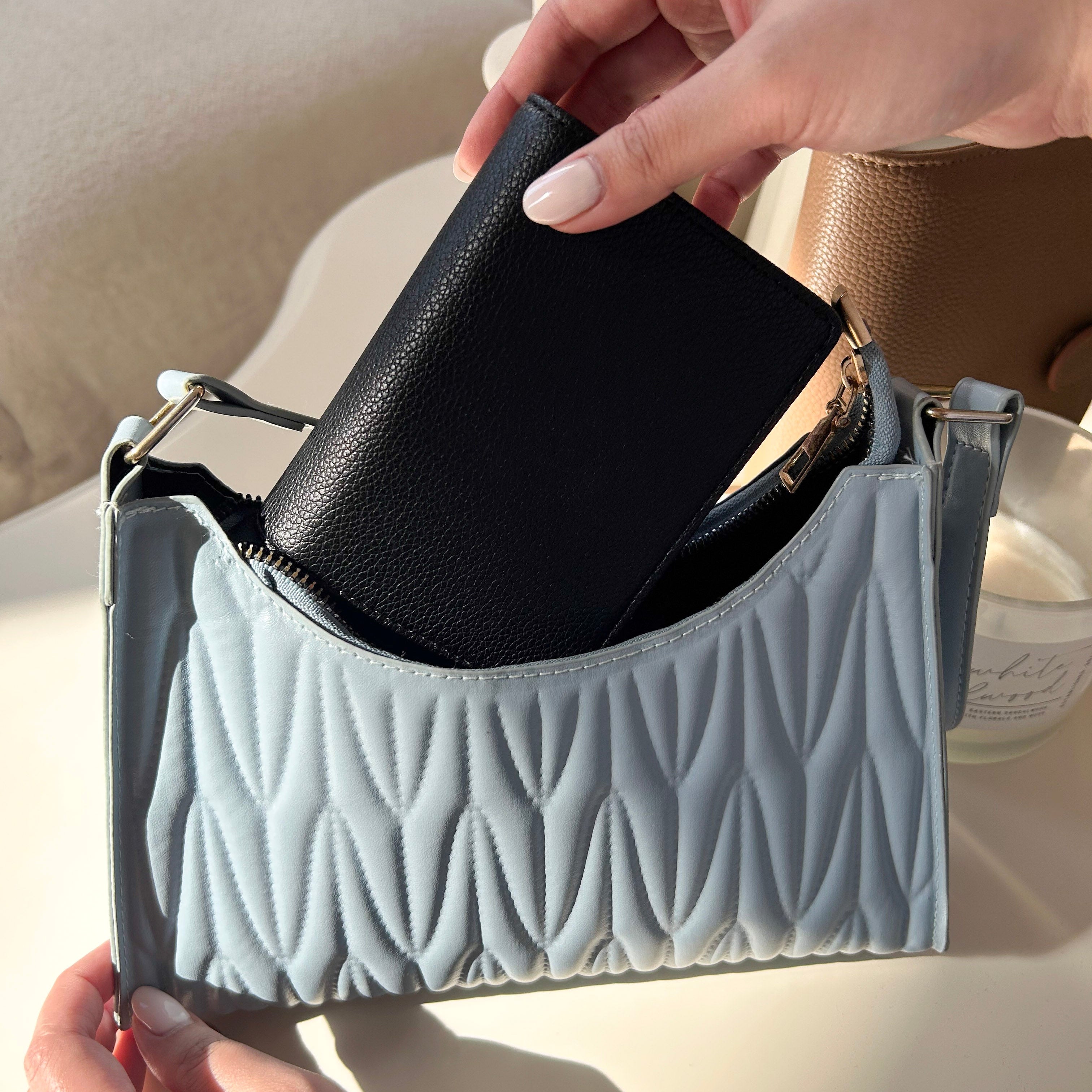 Person opening a quilted handbag with a black wallet.